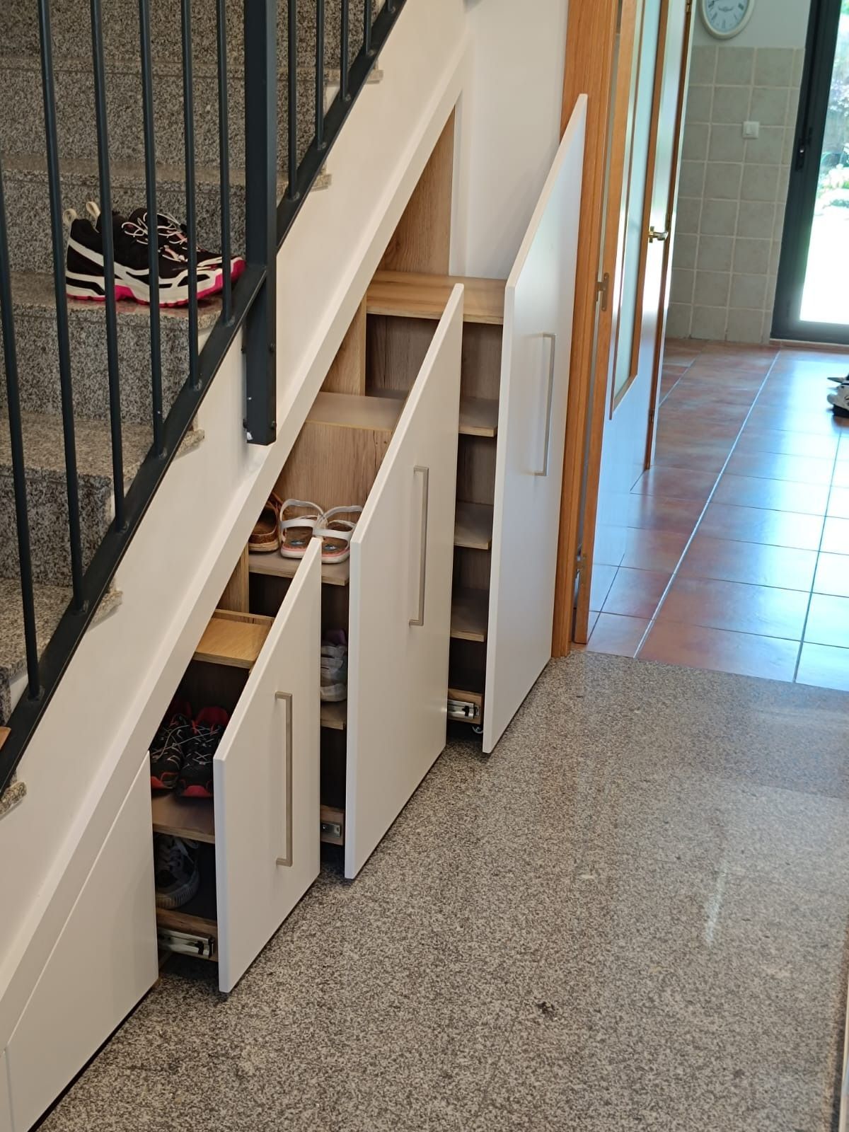 Armarios extraíbles blancos integrados en el espacio debajo de una escalera, utilizados para organizar el calzado.