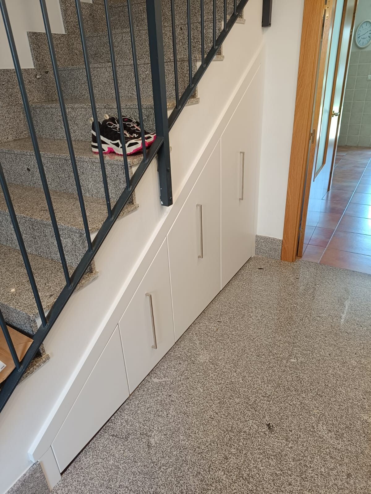 Armarios empotrados blancos instalados bajo una escalera de piedra en el interior de una vivienda con suelo de baldosas.