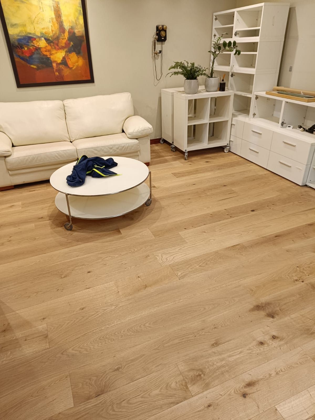 Un salón moderno con sofá blanco, mesa de centro redonda, suelo de madera clara y estanterías modulares blancas.