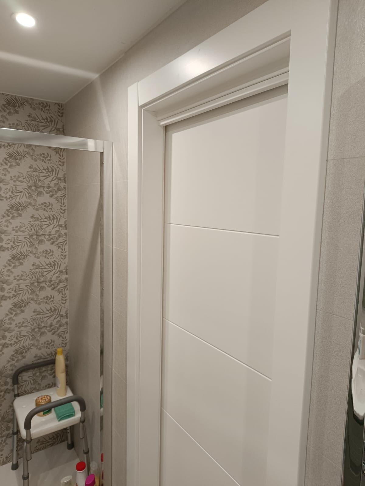 Una puerta interior blanca junto a una ducha a ras de suelo que contiene una silla de ducha para facilitar la asistencia.