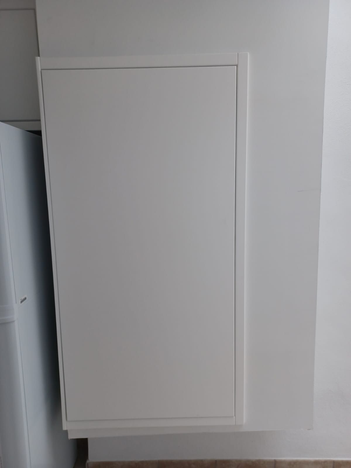 Una puerta de armario rectangular, blanca y sencilla, montada sobre una pared blanca en una cocina.