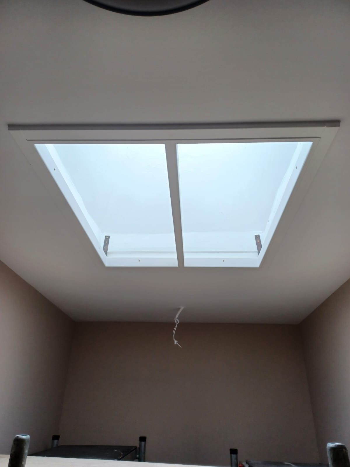 Una claraboya rectangular con un separador central instalada en una habitación con techo blanco y paredes beige.