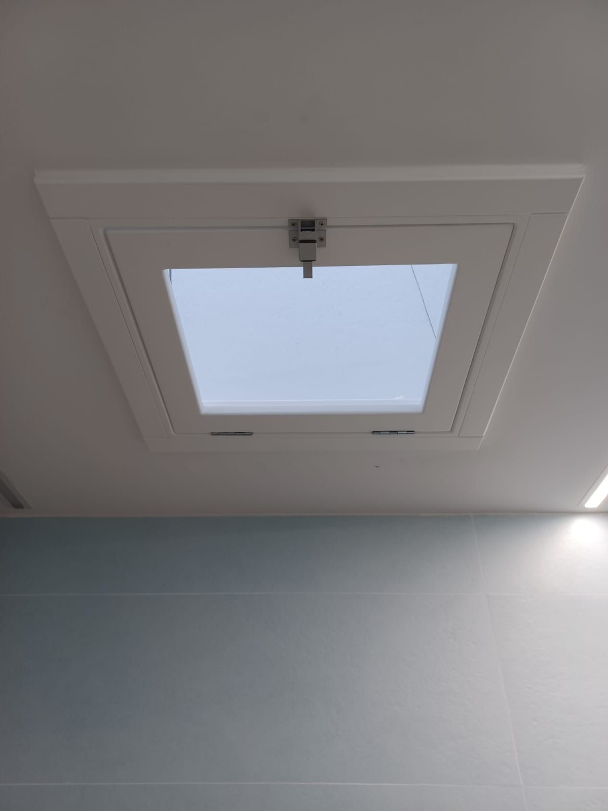 Una claraboya blanca integrada en un techo blanco liso, sobre una pared azul claro.