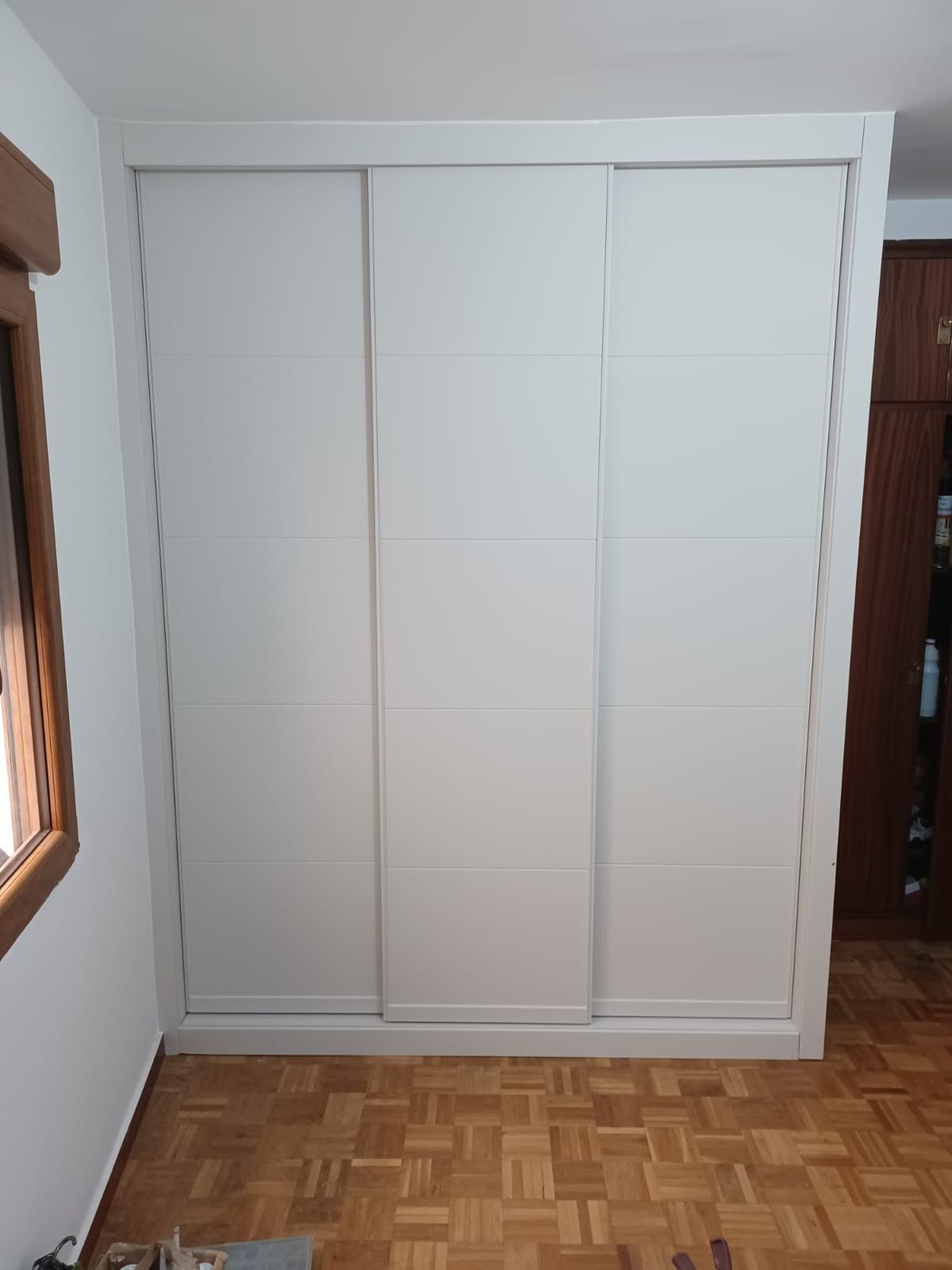 Un gran armario corredero blanco de tres paneles, colocado contra una pared con suelo de parqué de madera.