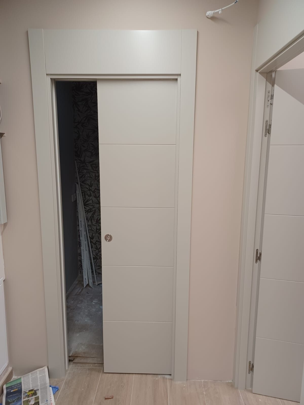 Una puerta corredera beige parcialmente abierta en un pasillo interior de color claro.