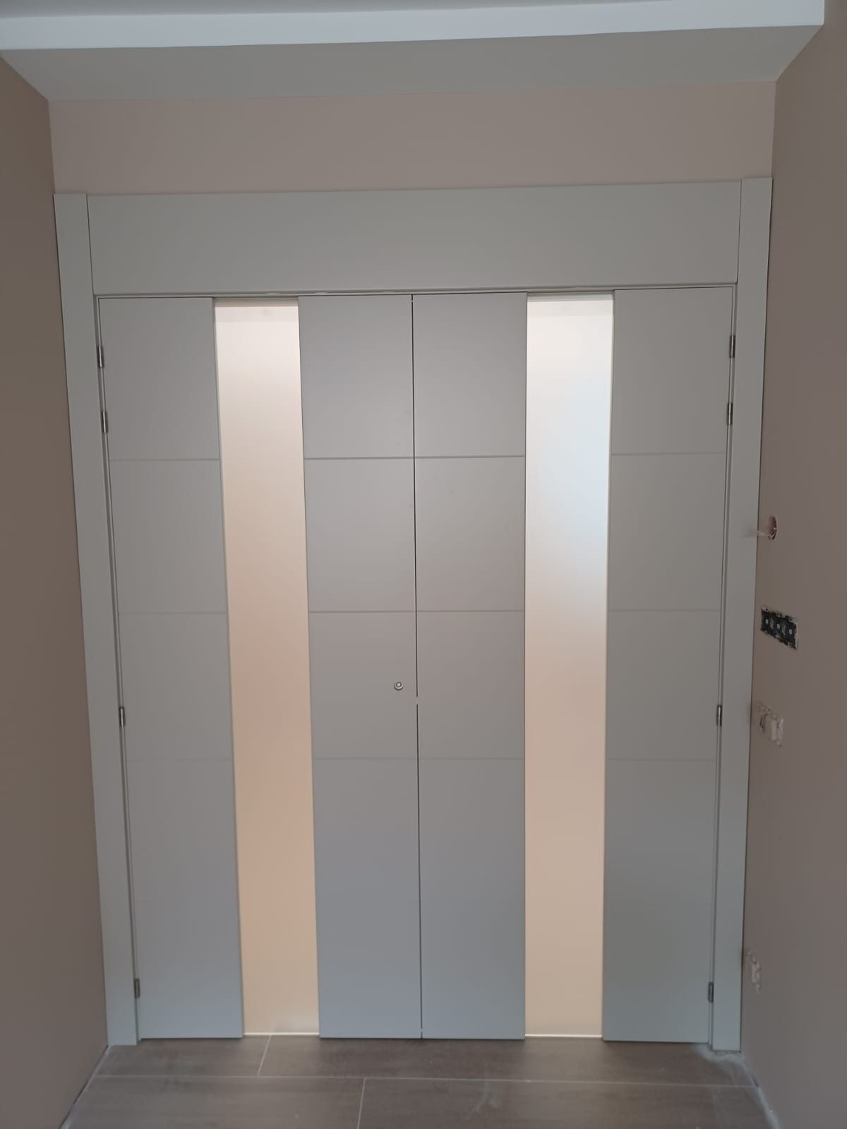 Un par de puertas dobles altas y de color claro, con paneles verticales de vidrio esmerilado y un diseño de cuadrícula.