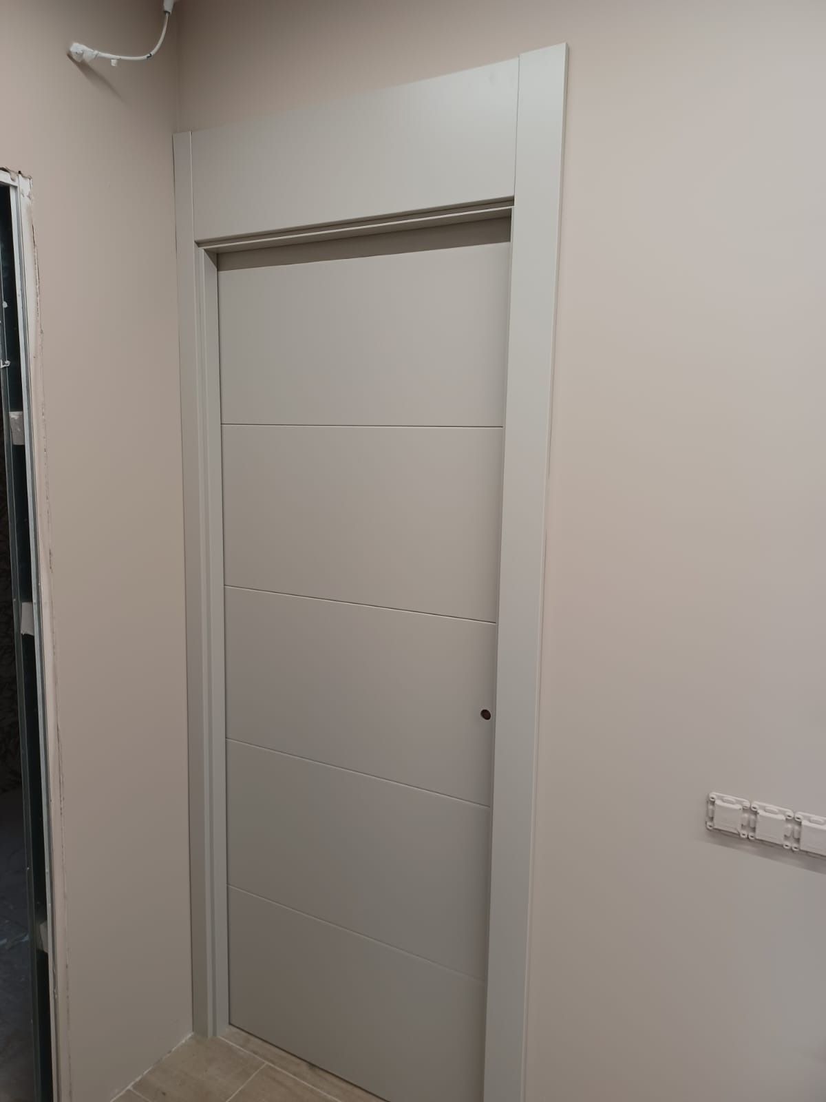 Una puerta gris claro con detalles de paneles horizontales, instalada en una pared de color claro con un marco a juego.