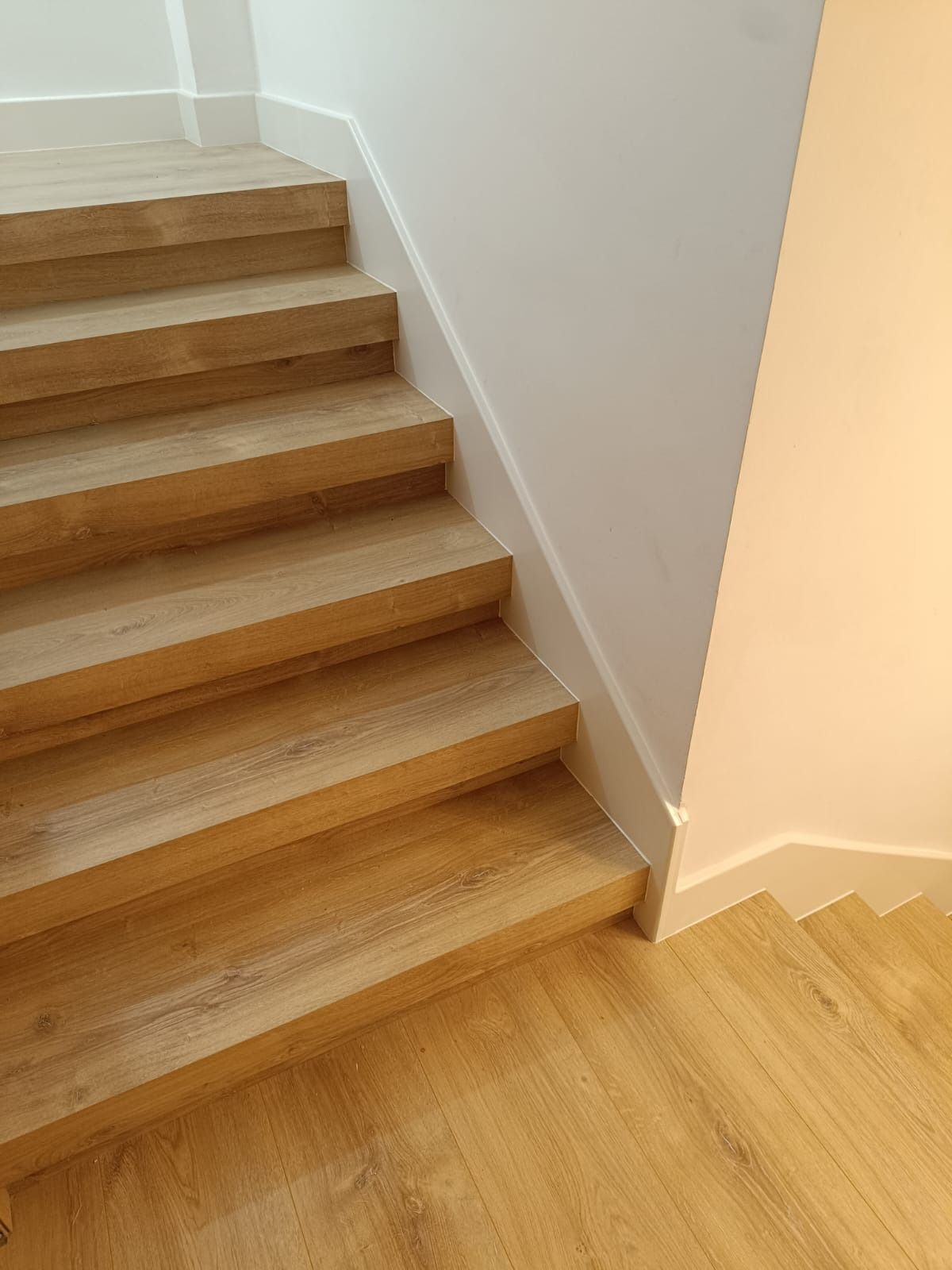 Una escalera de madera de roble claro con paredes y zócalos blancos.