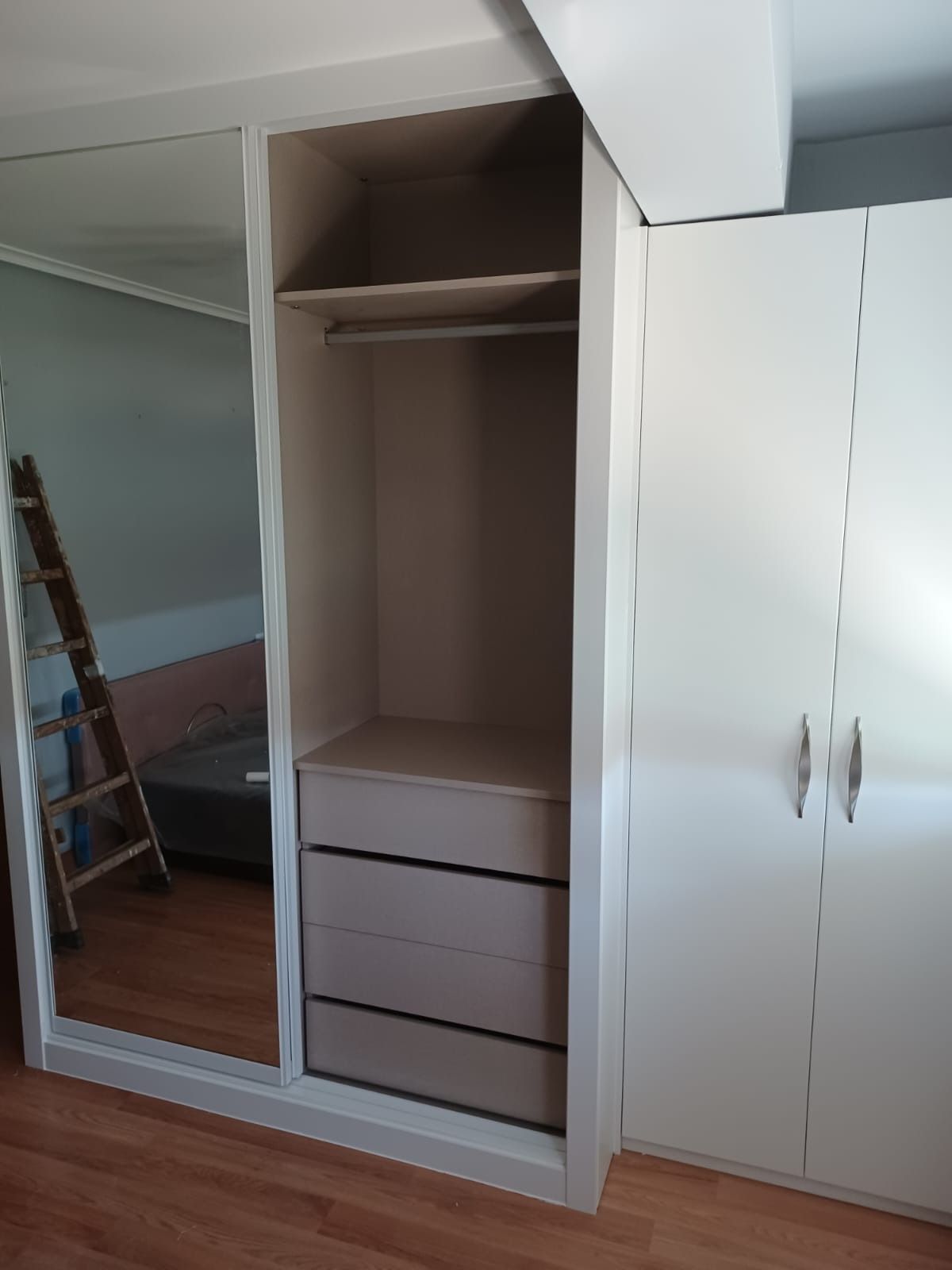 Un armario suspendido con puerta de espejo, sección central abierta con estantes y cajones, y puerta doble blanca.