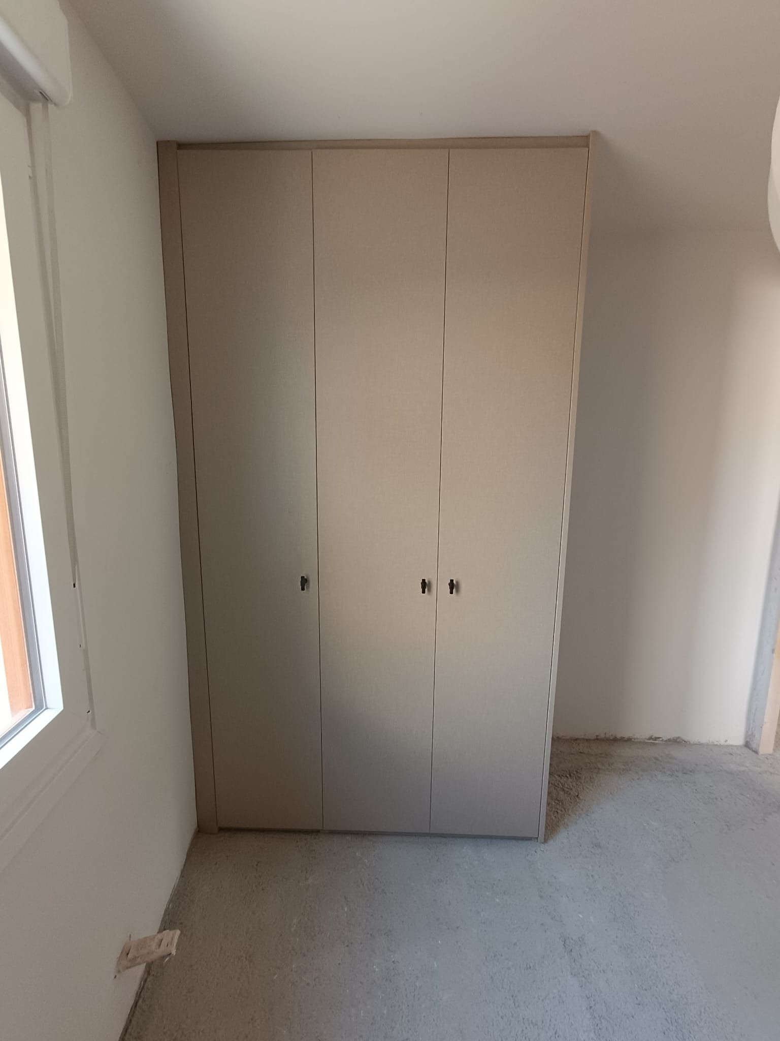 Un armario empotrado de tres puertas de color beige se alza 