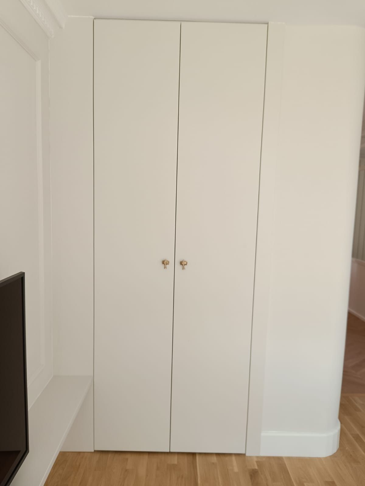 Armario blanco de doble puerta empotrado en la pared de una habitación con suelo de madera clara.