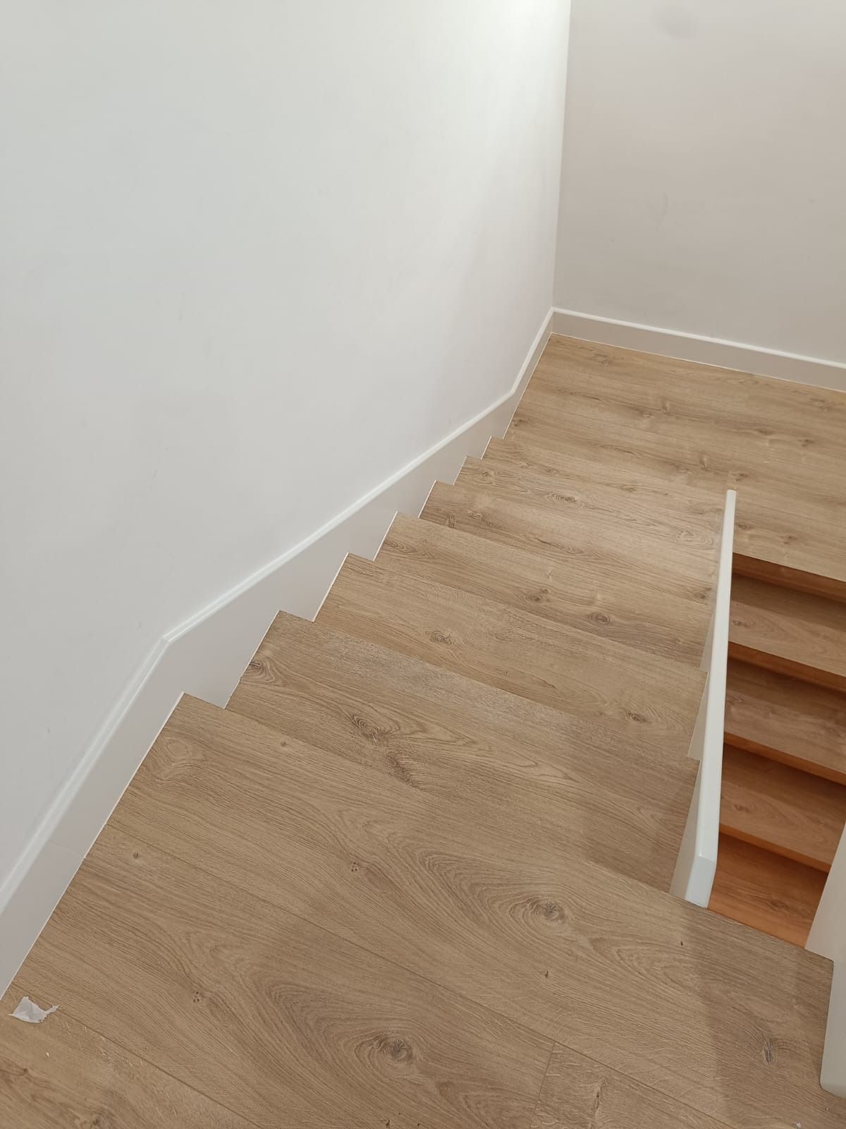 Vista desde un ángulo elevado de una escalera de madera con paredes y zócalos blancos.