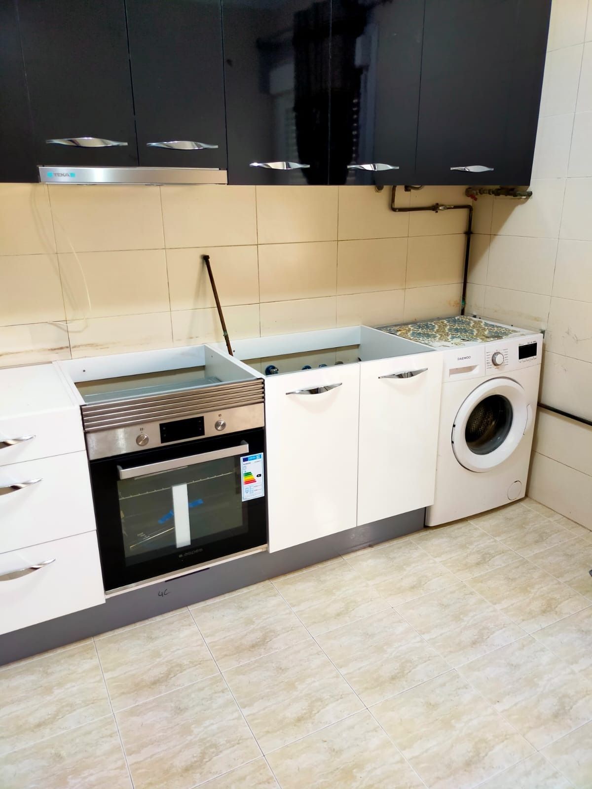 Una cocina moderna con armarios superiores negros, armarios inferiores blancos, horno empotrado y lavadora blanca.