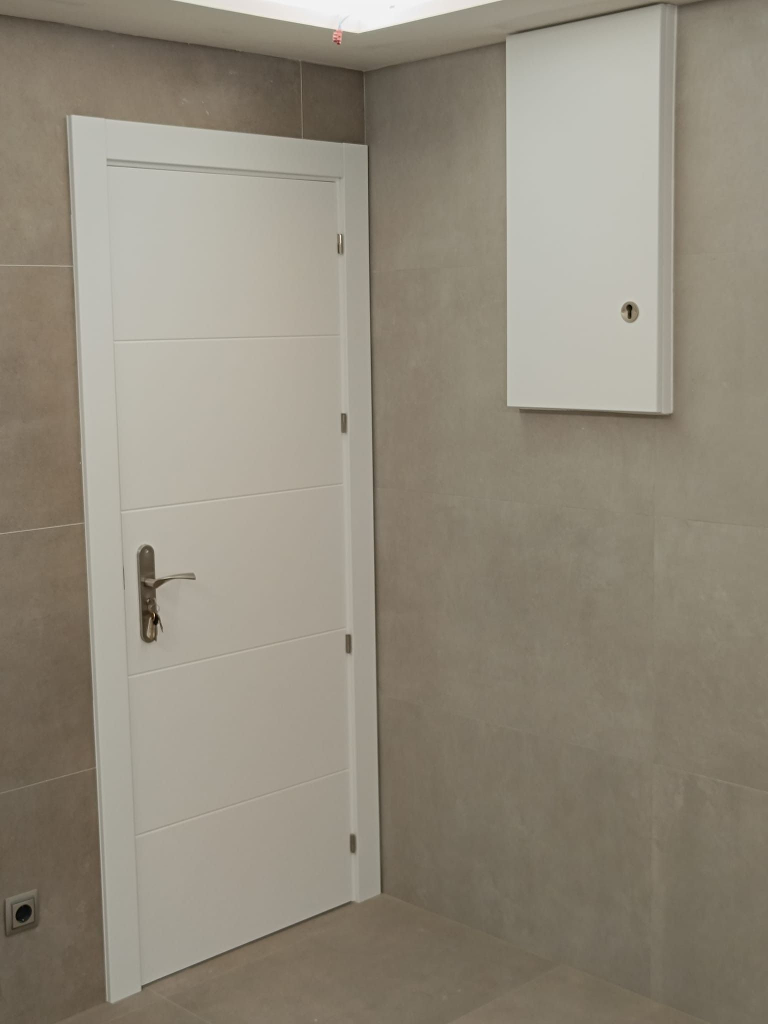 Una puerta blanca y un pequeño armario blanco en una pared de azulejos grises dentro de una habitación.