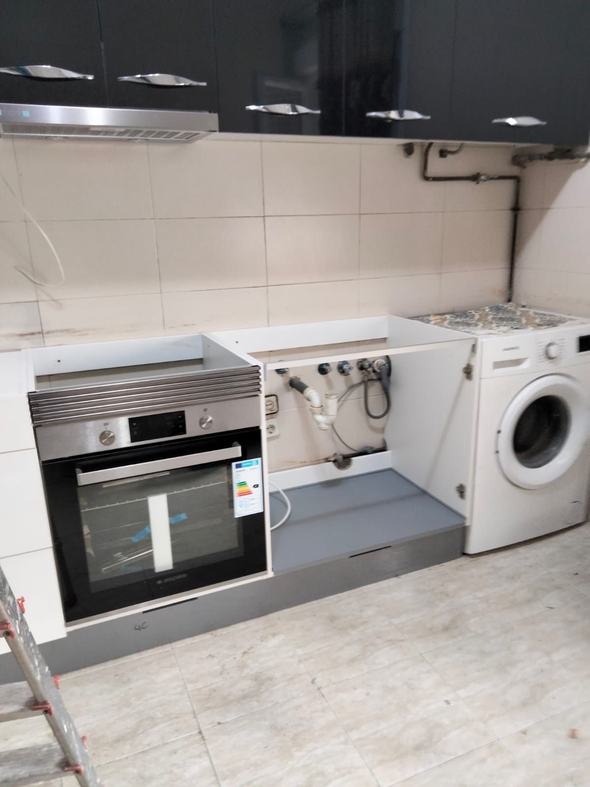 Una cocina en construcción con horno empotrado, tuberías a la vista, espacio para un fregadero y lavadora blanca.
