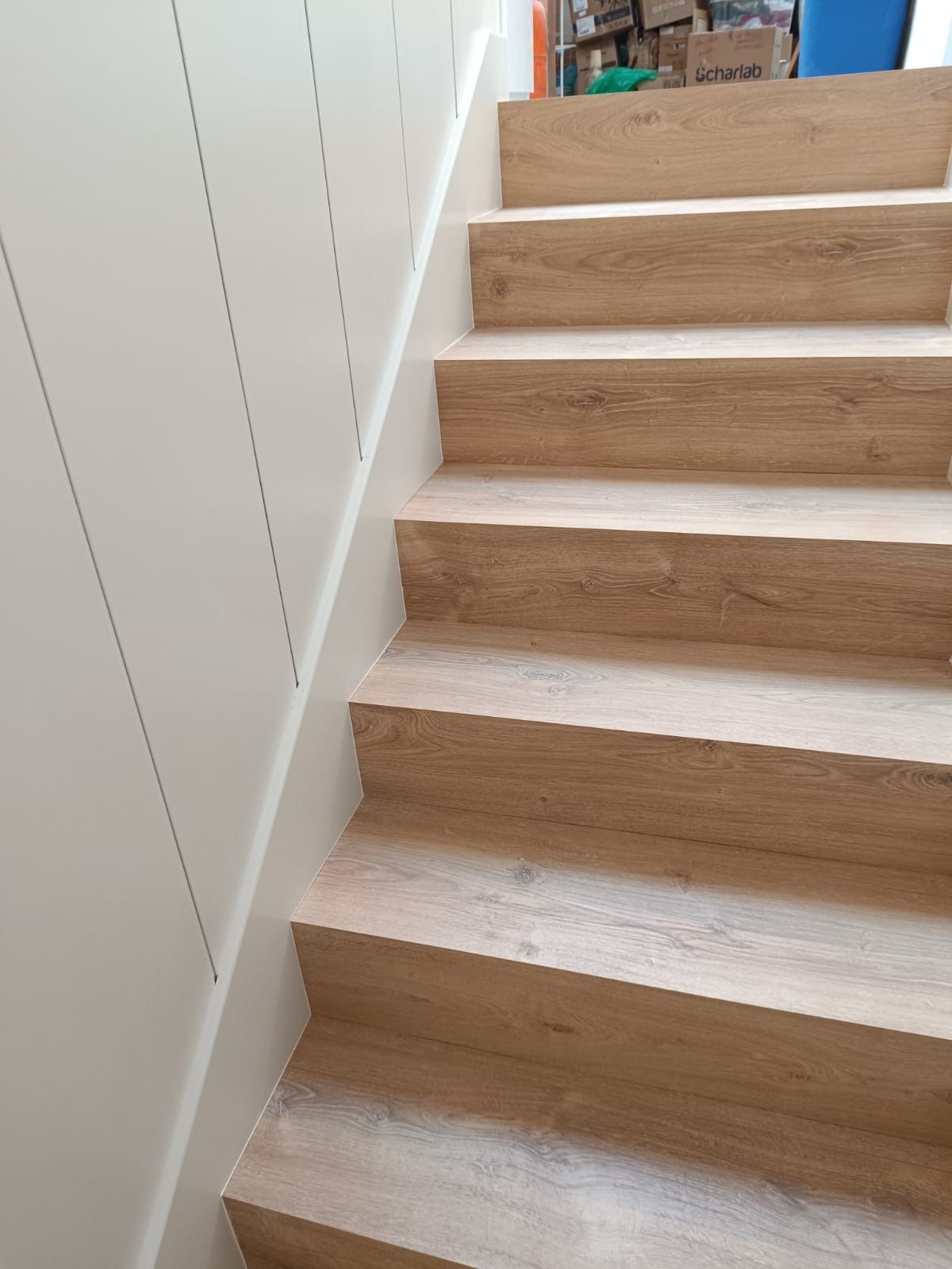 Una escalera de madera clara junto a una pared con paneles verticales blancos.