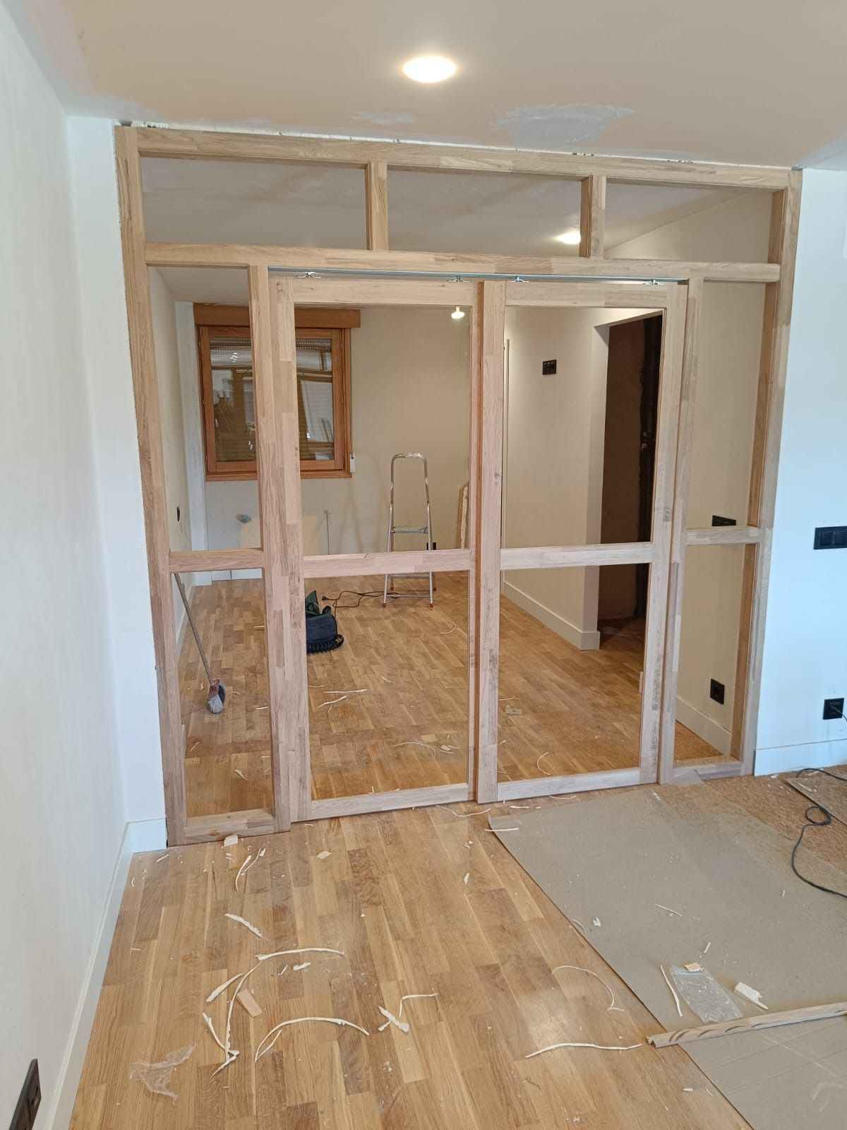 Estructura de madera para un tabique con puertas dobles, en construcción en una habitación con suelo de madera noble.