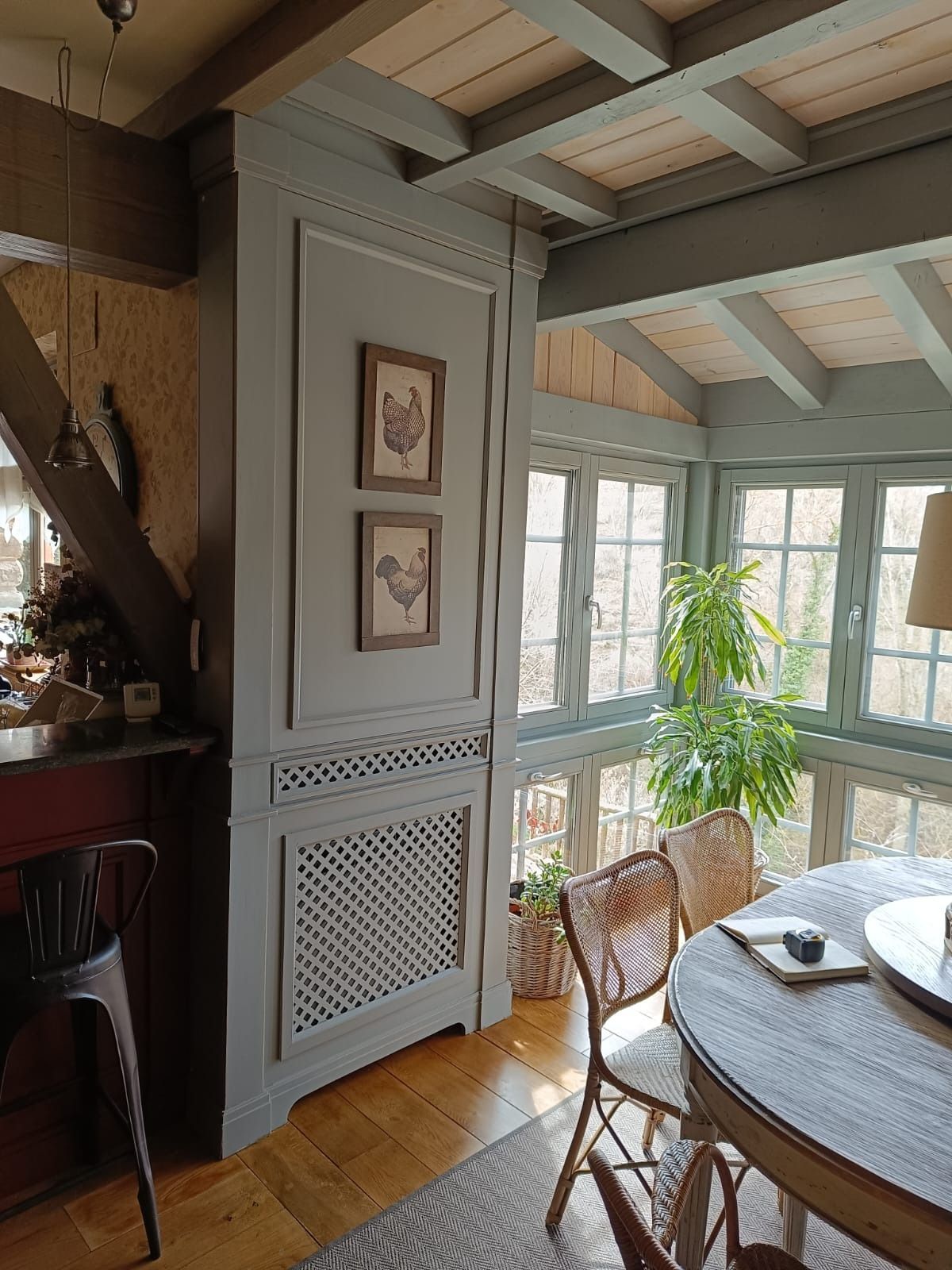 Un comedor con una cubierta de radiador gris con motivos de celosía, dos cuadros enmarcados y una mesa redonda de madera.