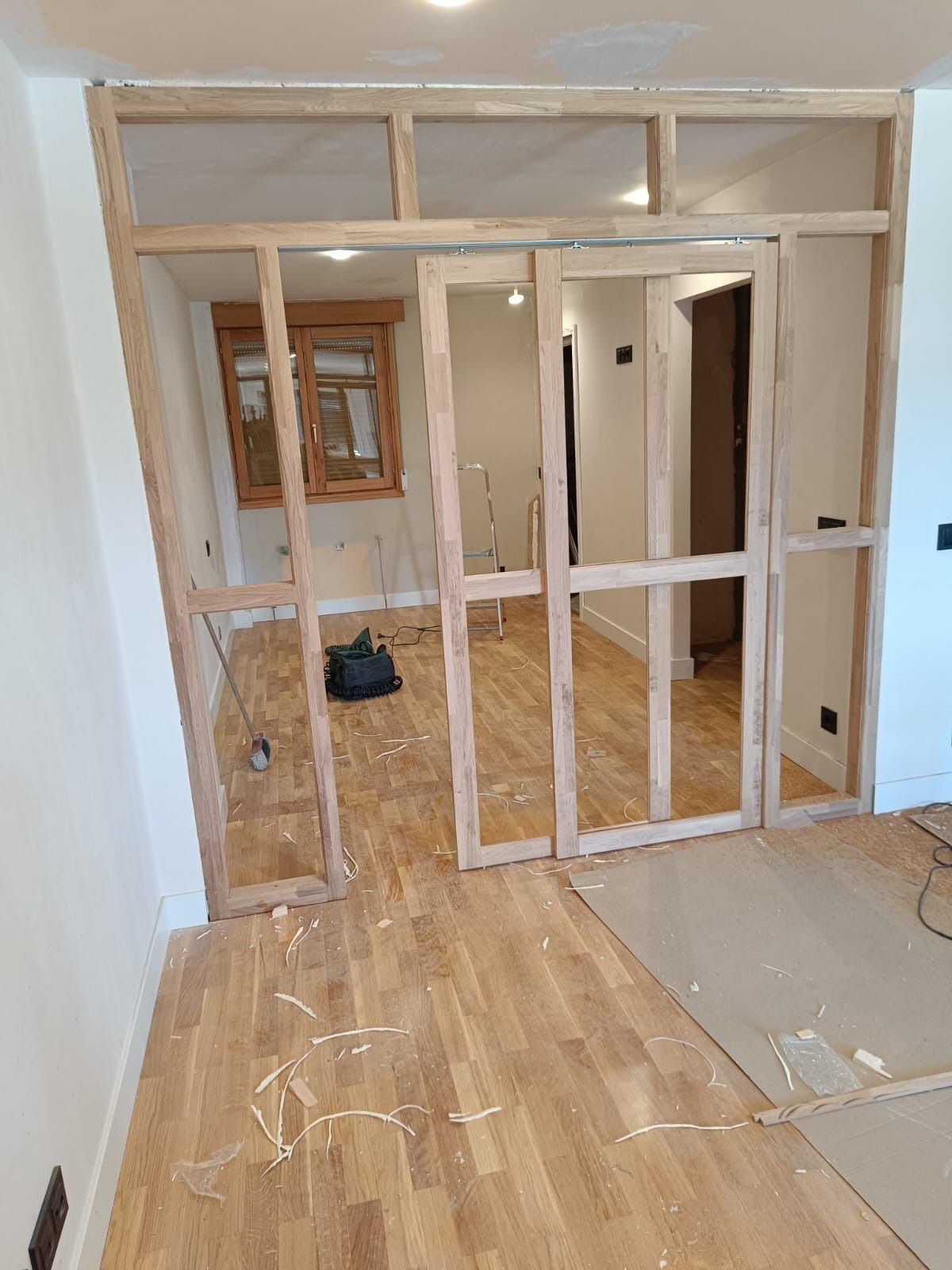 Un tabique con estructura de madera y una puerta en construcción en una habitación con suelo de madera noble.