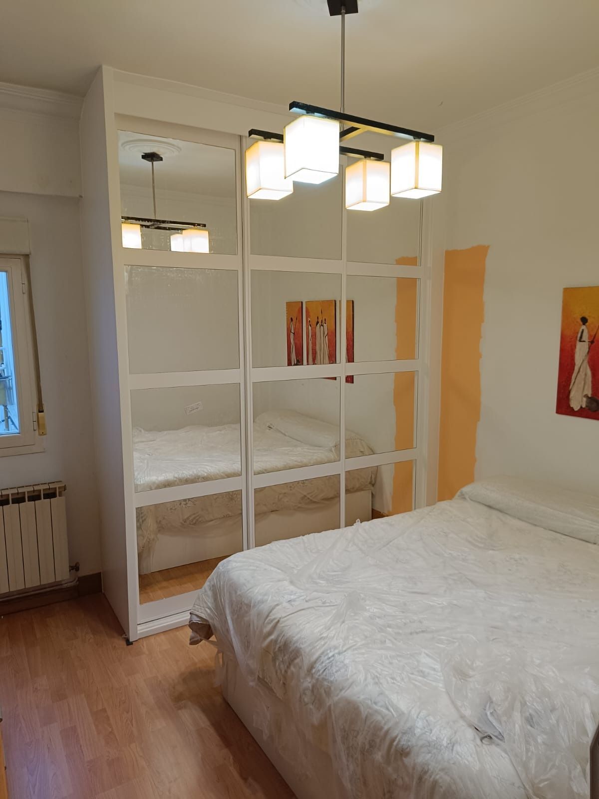 Un dormitorio con un gran armario con espejos, una cama con ropa de cama blanca, suelo de madera y una lámpara moderna.