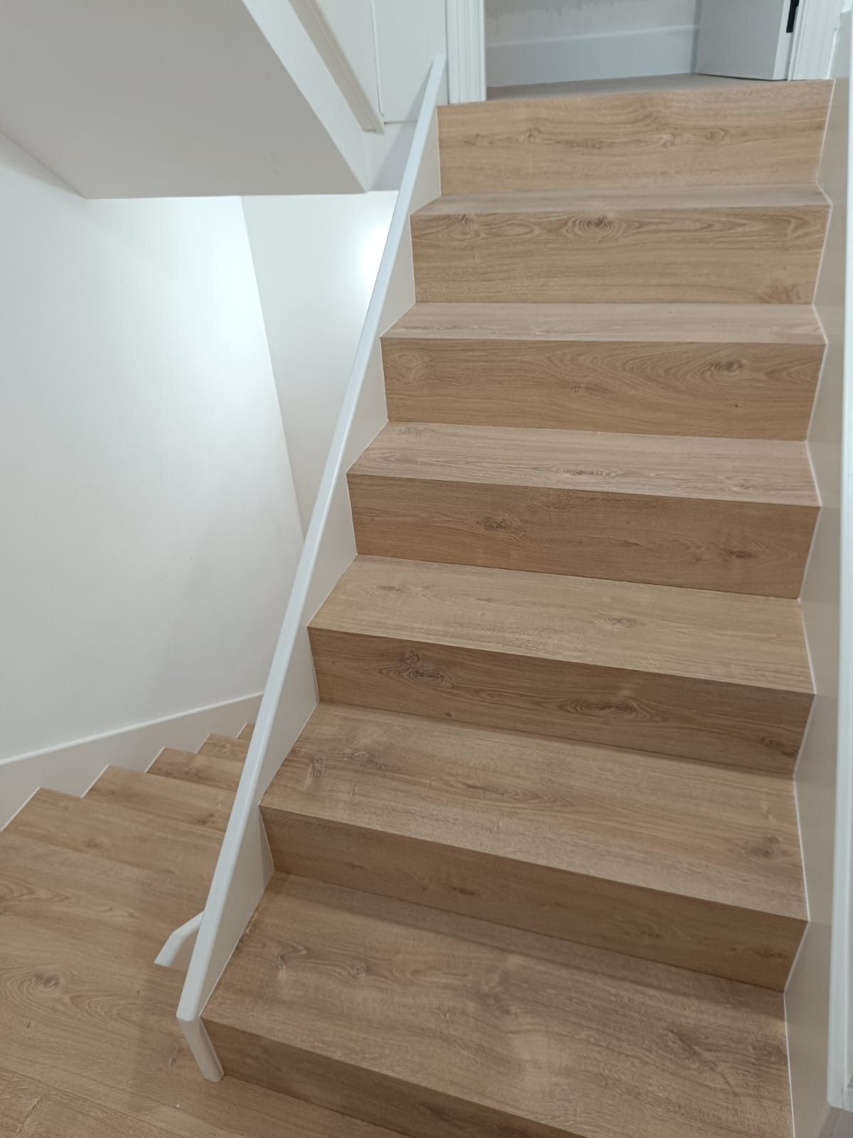 Una escalera de madera con paredes y molduras blancas, que conduce tanto hacia arriba como hacia abajo.