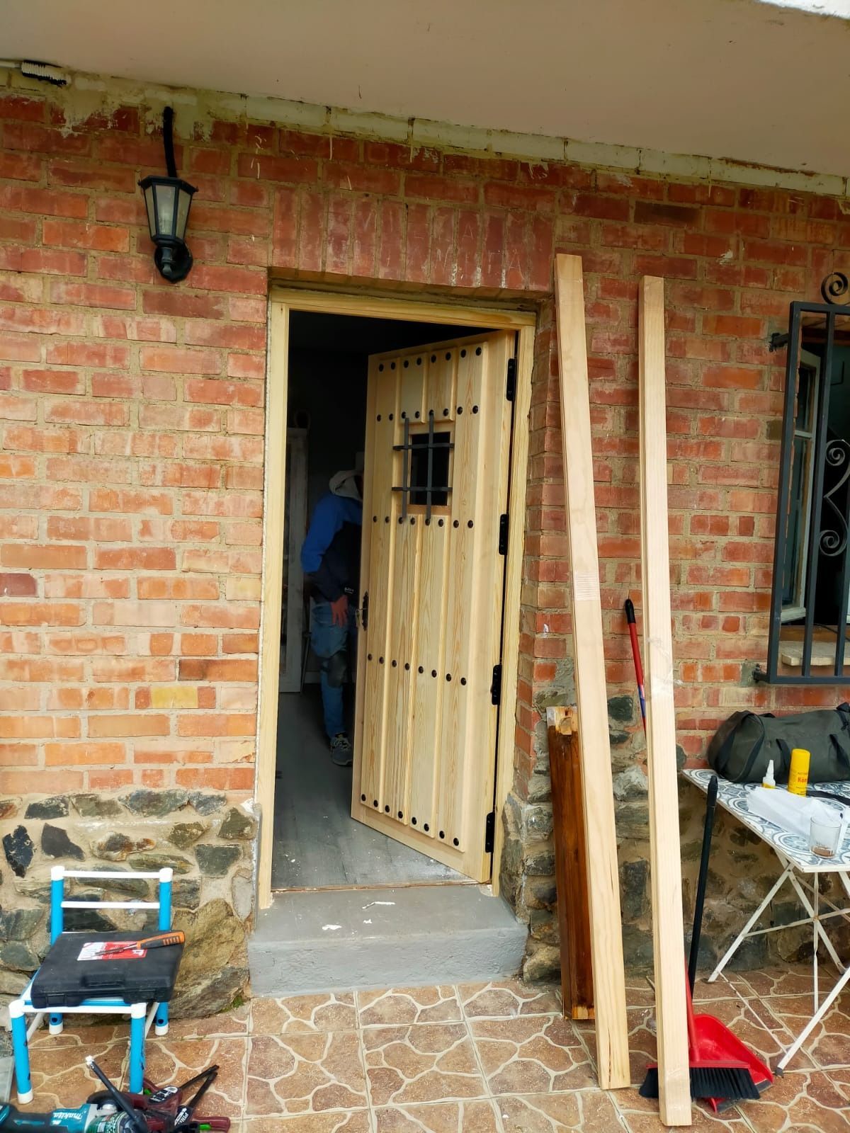 Una persona se encuentra dentro de la entrada de un edificio de ladrillo donde se está instalando una nueva puerta de madera.