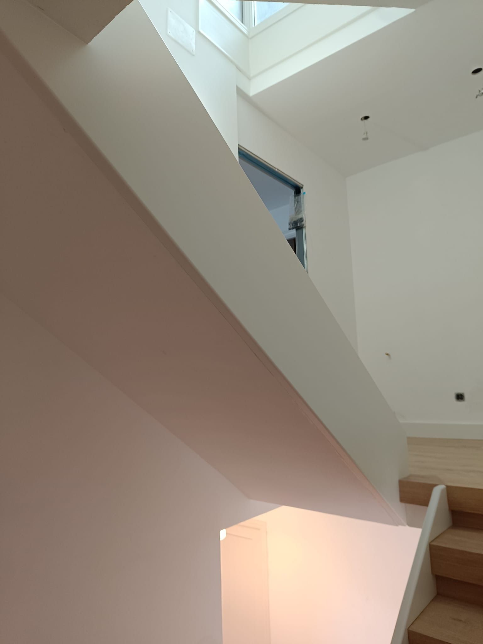 Escalera interior moderna con peldaños de madera, una pared blanca inclinada y una claraboya en el techo.