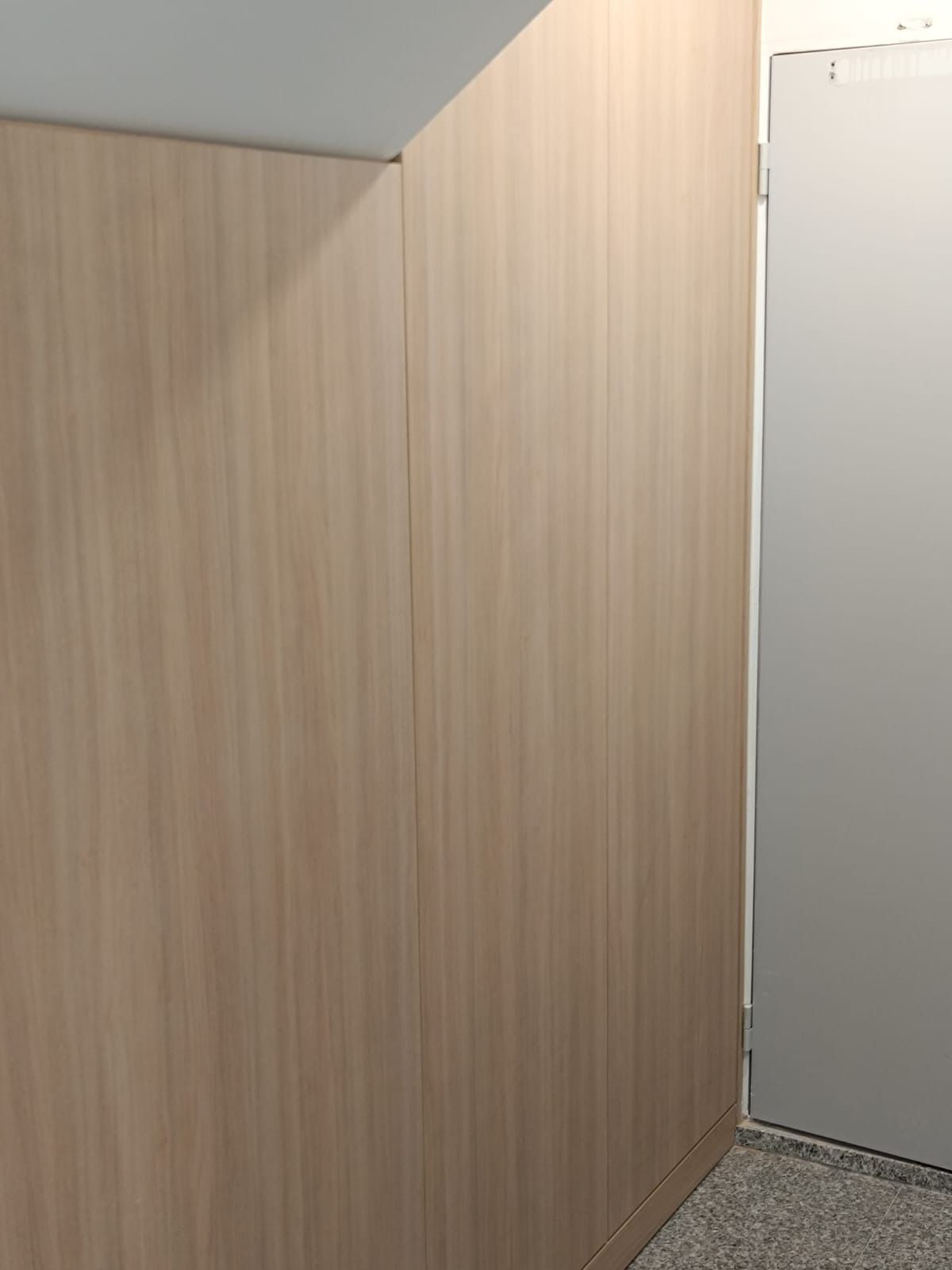 Un revestimiento de madera clara cubre una pared, dando paso a un marco de puerta blanco en el lado derecho.