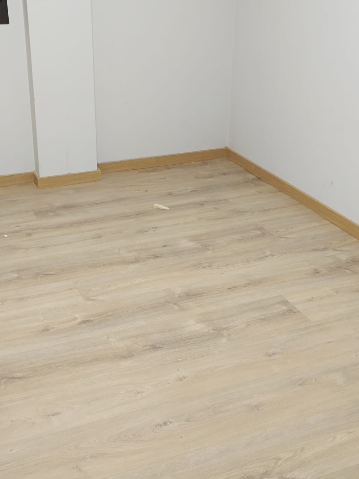 Suelo de madera clara con zócalos a juego en la esquina de una habitación con paredes blancas.