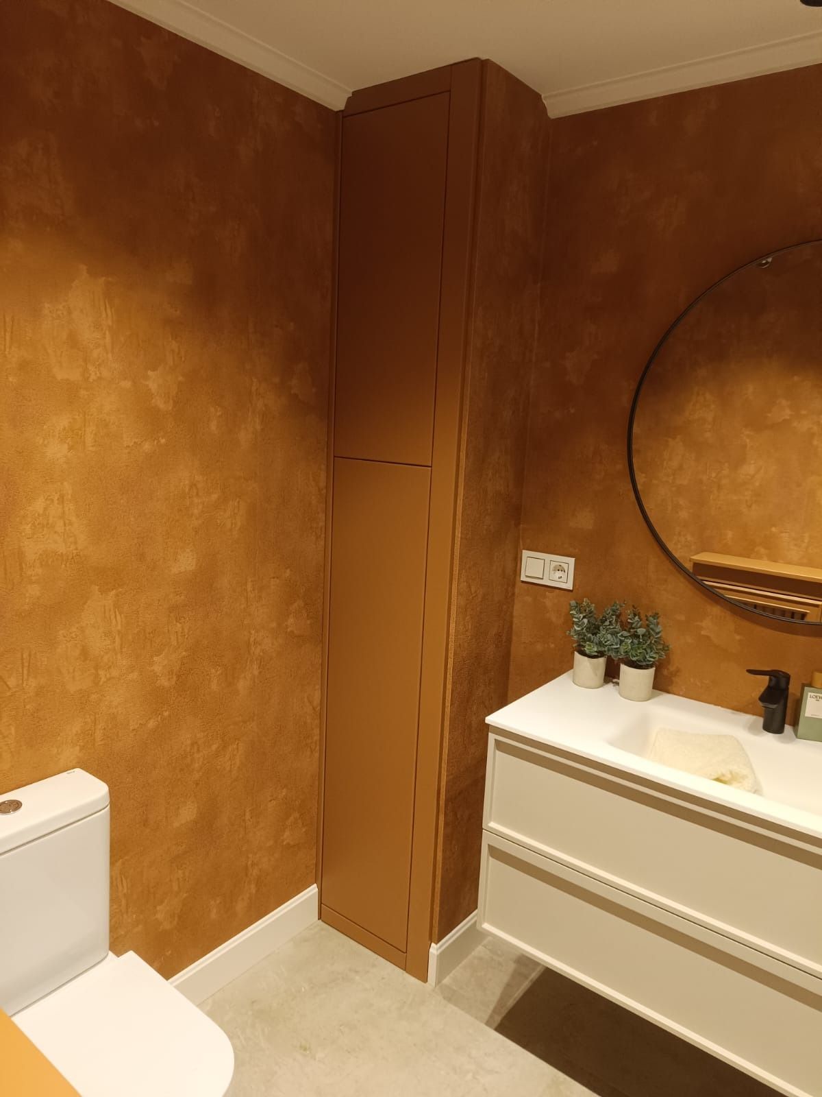 Un baño pequeño con paredes texturizadas de color cobre, un tocador flotante blanco con lavabo y un armario alto a juego.