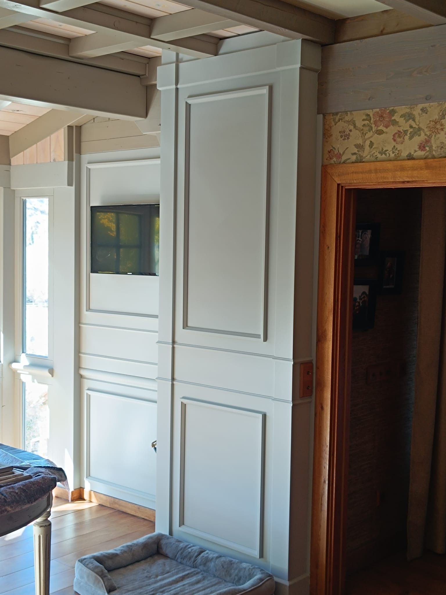 Pared gris claro con paneles decorativos y un hueco empotrado para la televisión junto a un marco de puerta de madera.