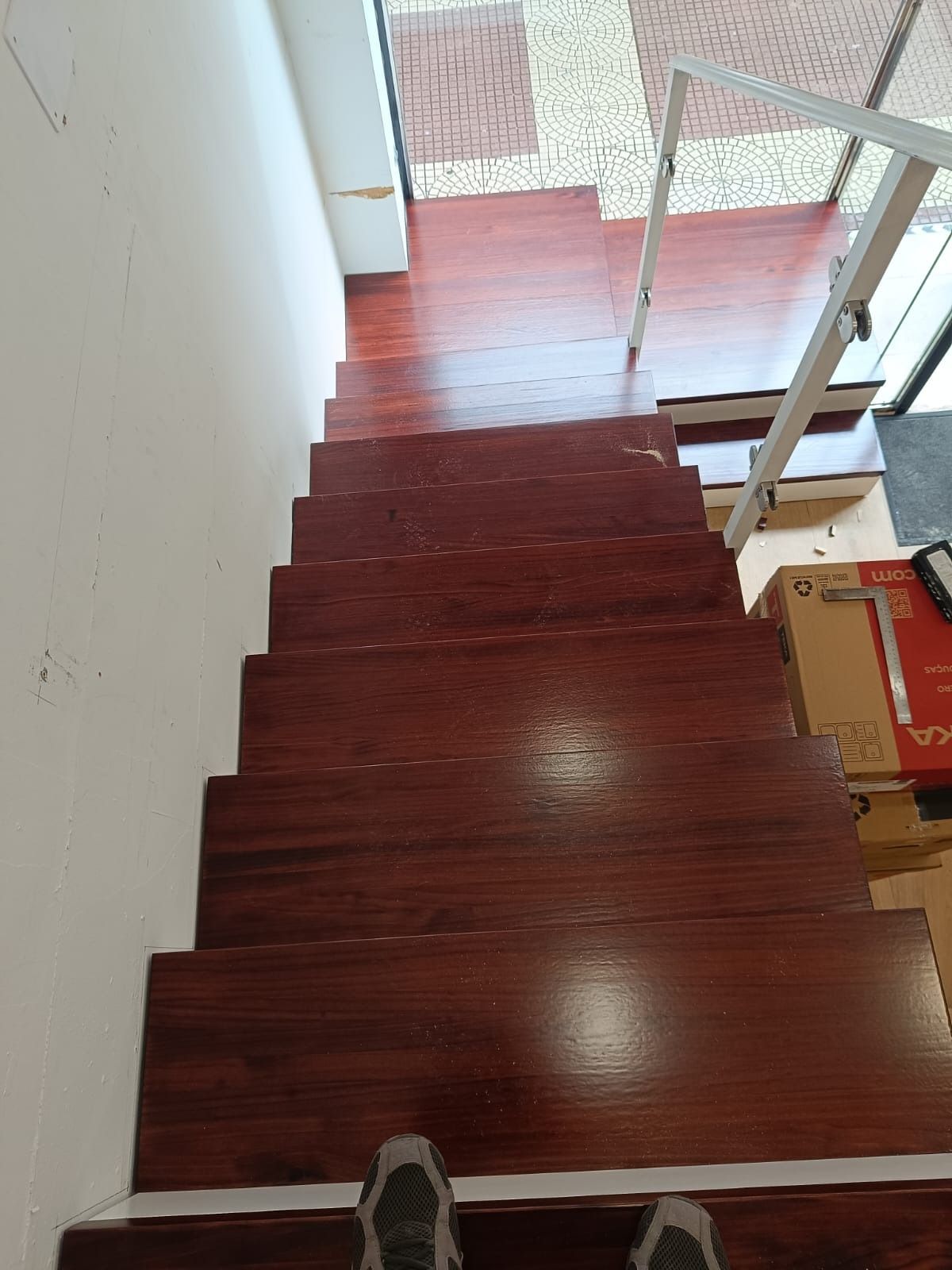 Vista de una empinada y estrecha escalera de madera con peldaños de color marrón rojizo oscuro en un interior bien iluminado.