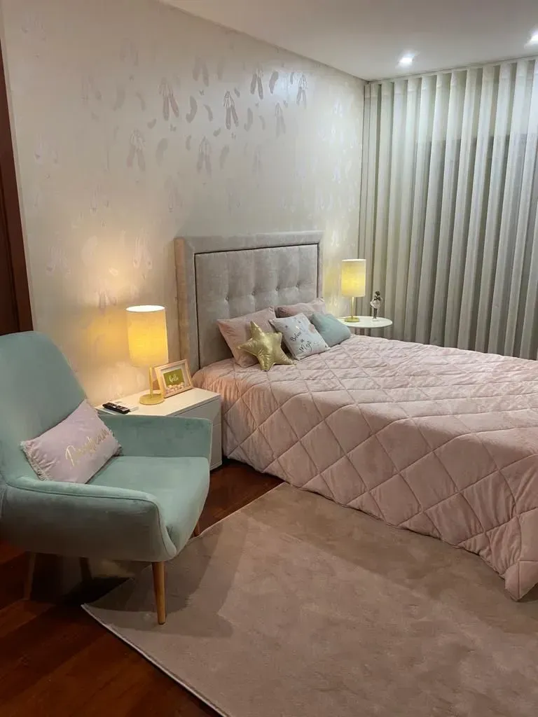 Um quarto com uma cama, cadeira, lâmpadas e cortinas.