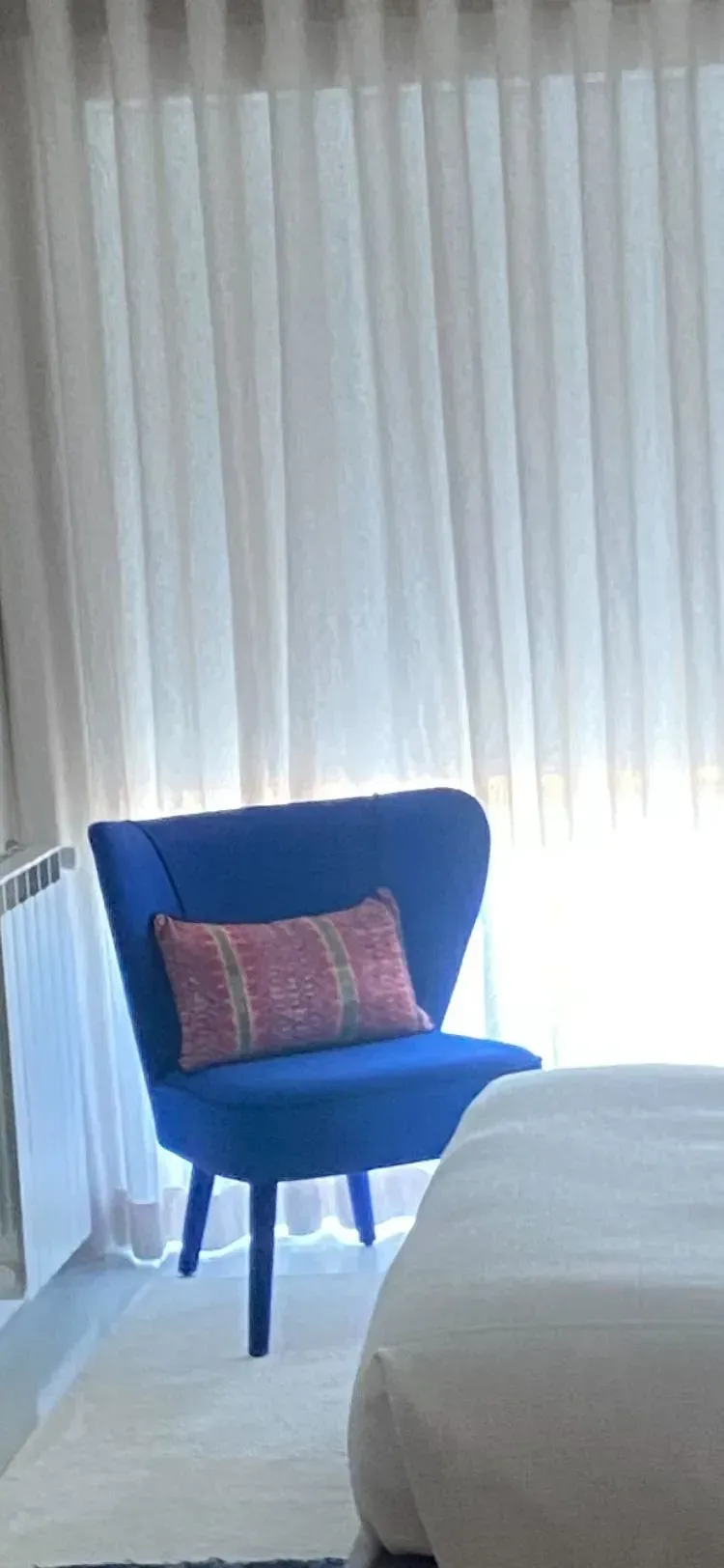 Uma cadeira azul com uma almofada rosa está ao lado de uma cama em um quarto de hotel.