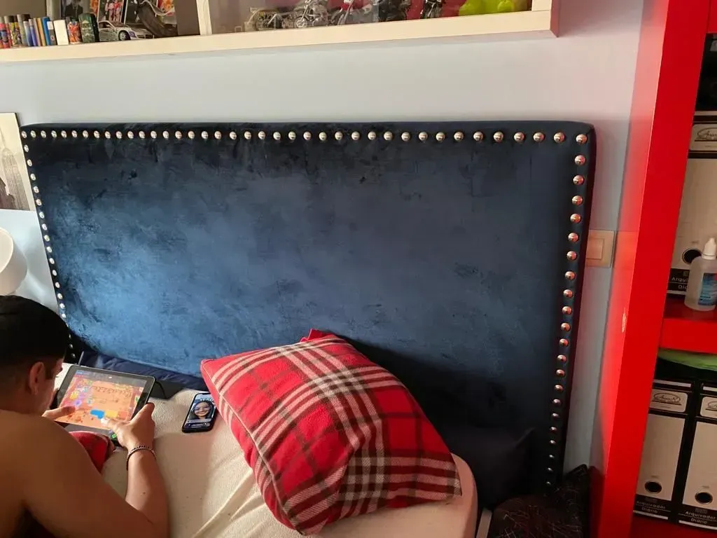 Um homem está deitado em uma cama com cabeceira azul e um travesseiro vermelho.