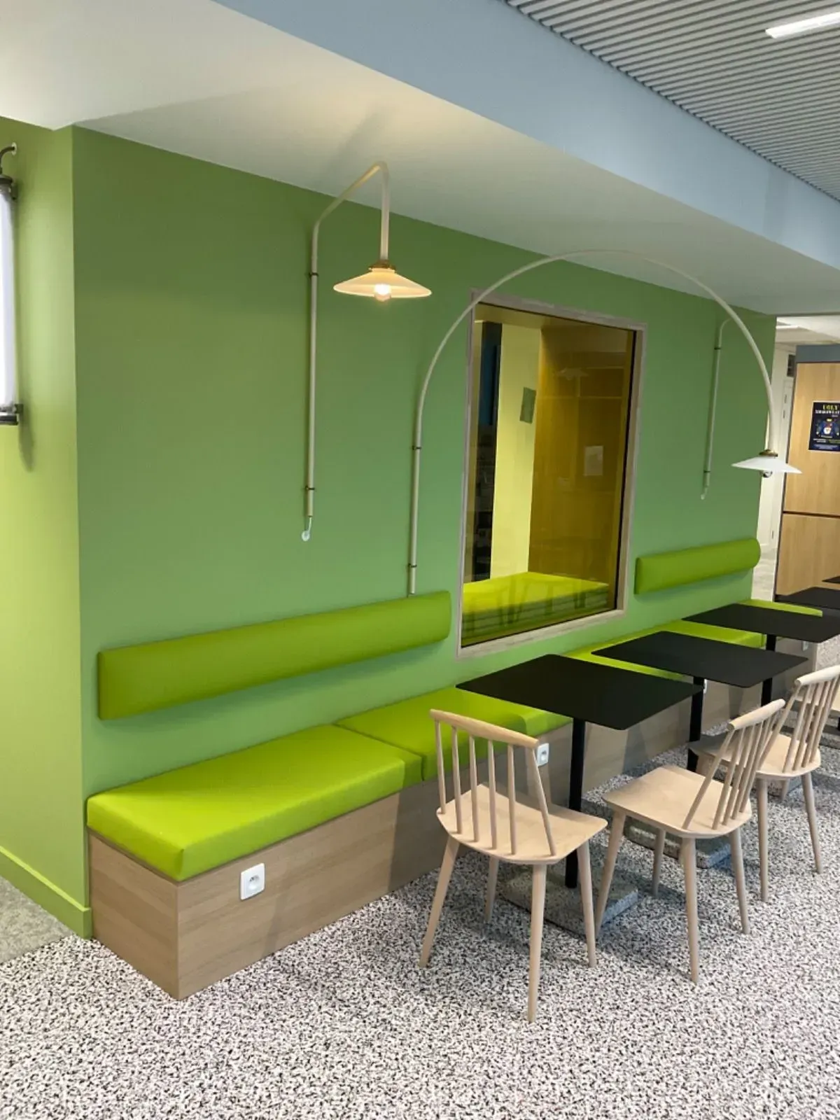 Uma sala com paredes verdes, cadeiras, mesas e um banco.