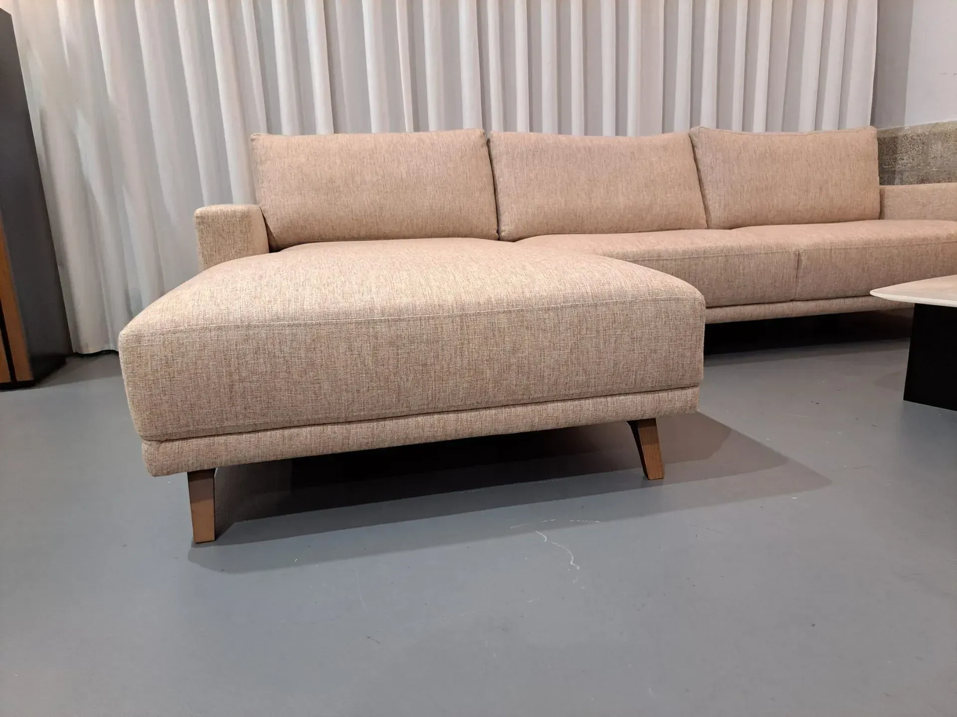 Um sofá secional bege está em uma sala de estar ao lado de uma mesa de centro.