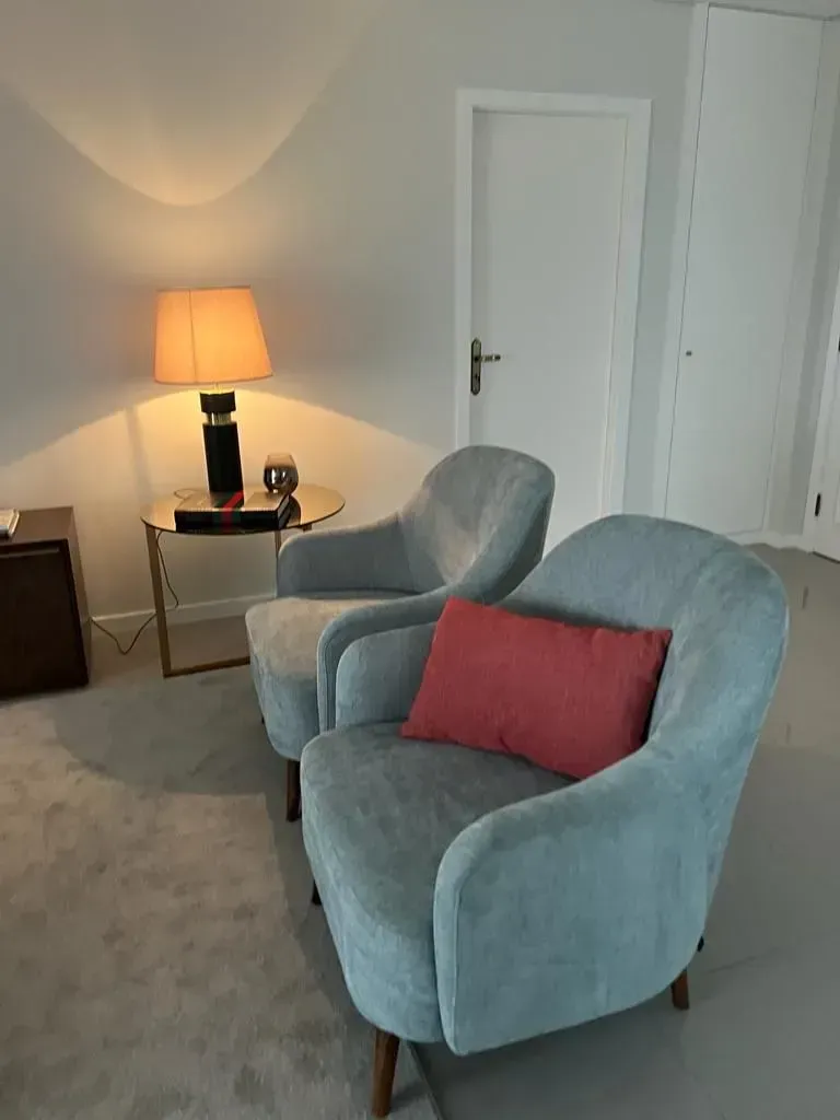 Uma sala de estar com duas cadeiras, uma mesa e um abajur.