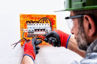 Un hombre que lleva casco y guantes está trabajando en una caja eléctrica.