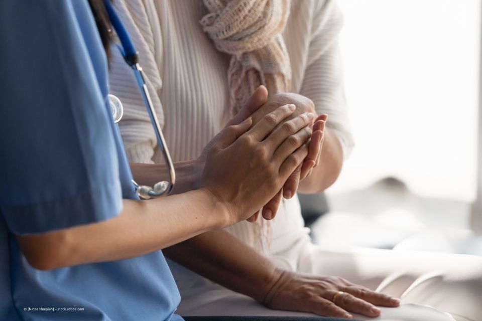 Eine medizinische Fachkraft in blauer OP-Kleidung hält die Hände einer Person, die einen Schal trägt.