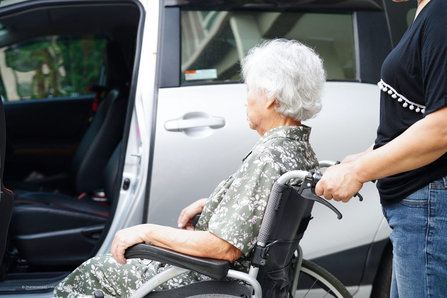 Eine Person im Rollstuhl wird von einer anderen Person in ein Auto geholfen. Die Autotür ist geöffnet.