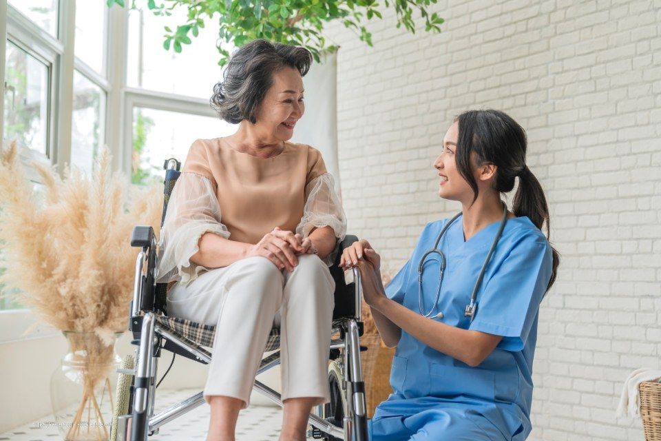 Frau im Rollstuhl lächelt medizinischem Fachpersonal zu, Hände berühren sich, Innenraum.
