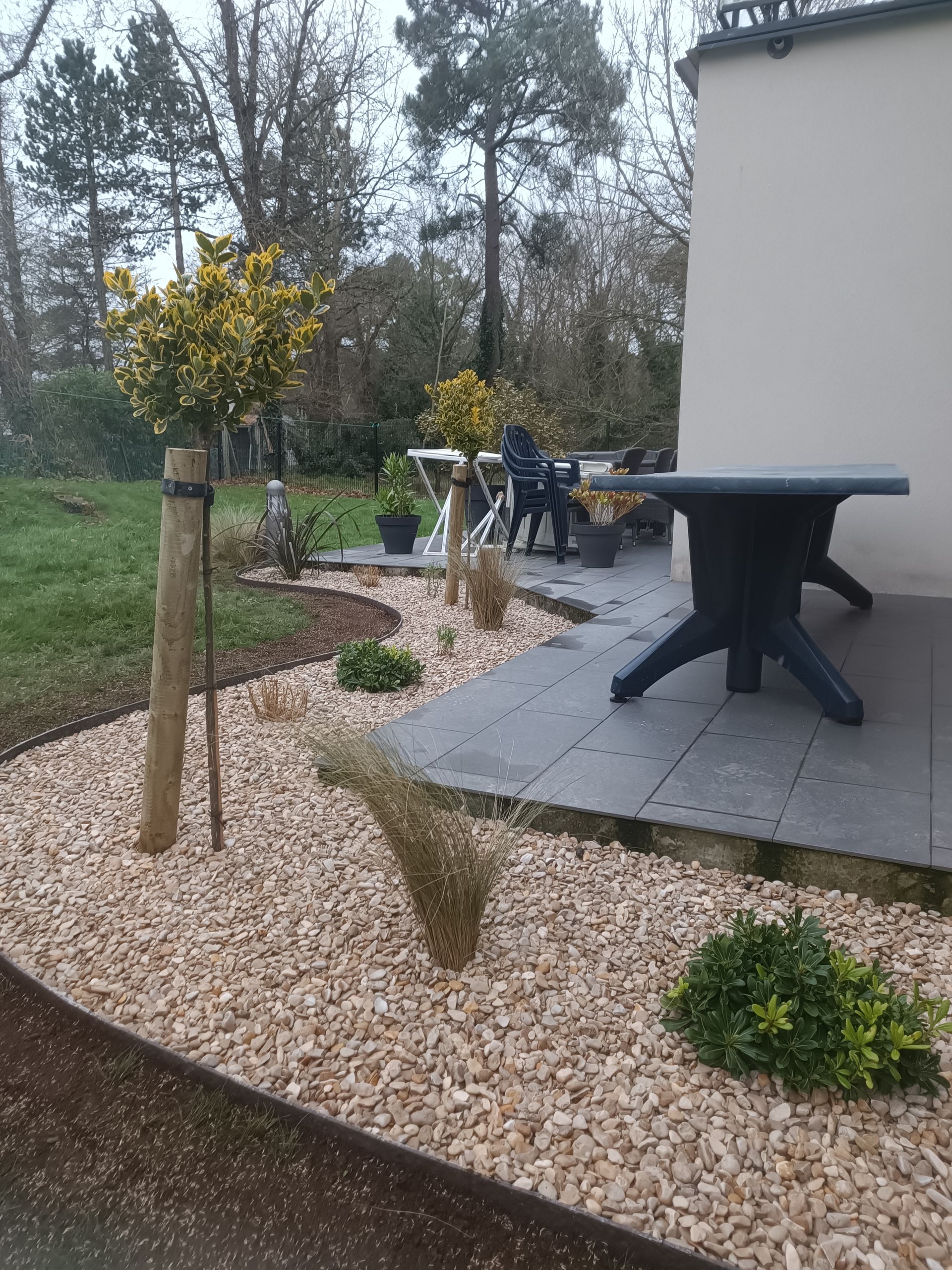 Un coin aménagé avec des graviers, un banc et une table sous un arbre