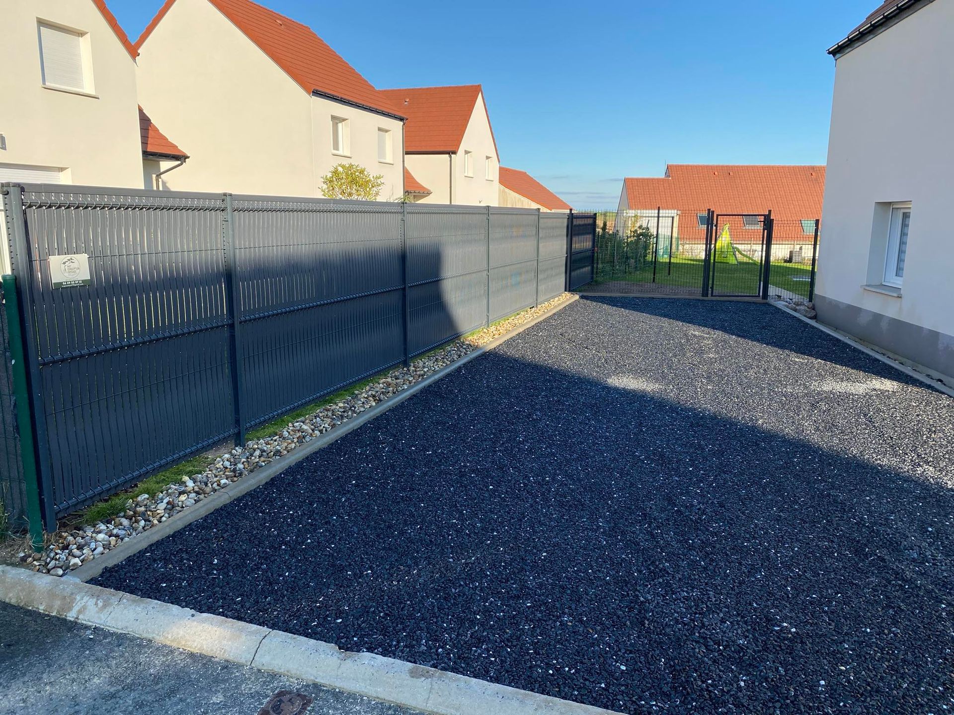 Une allée avec du gravier noir et une clôture moderne en métal