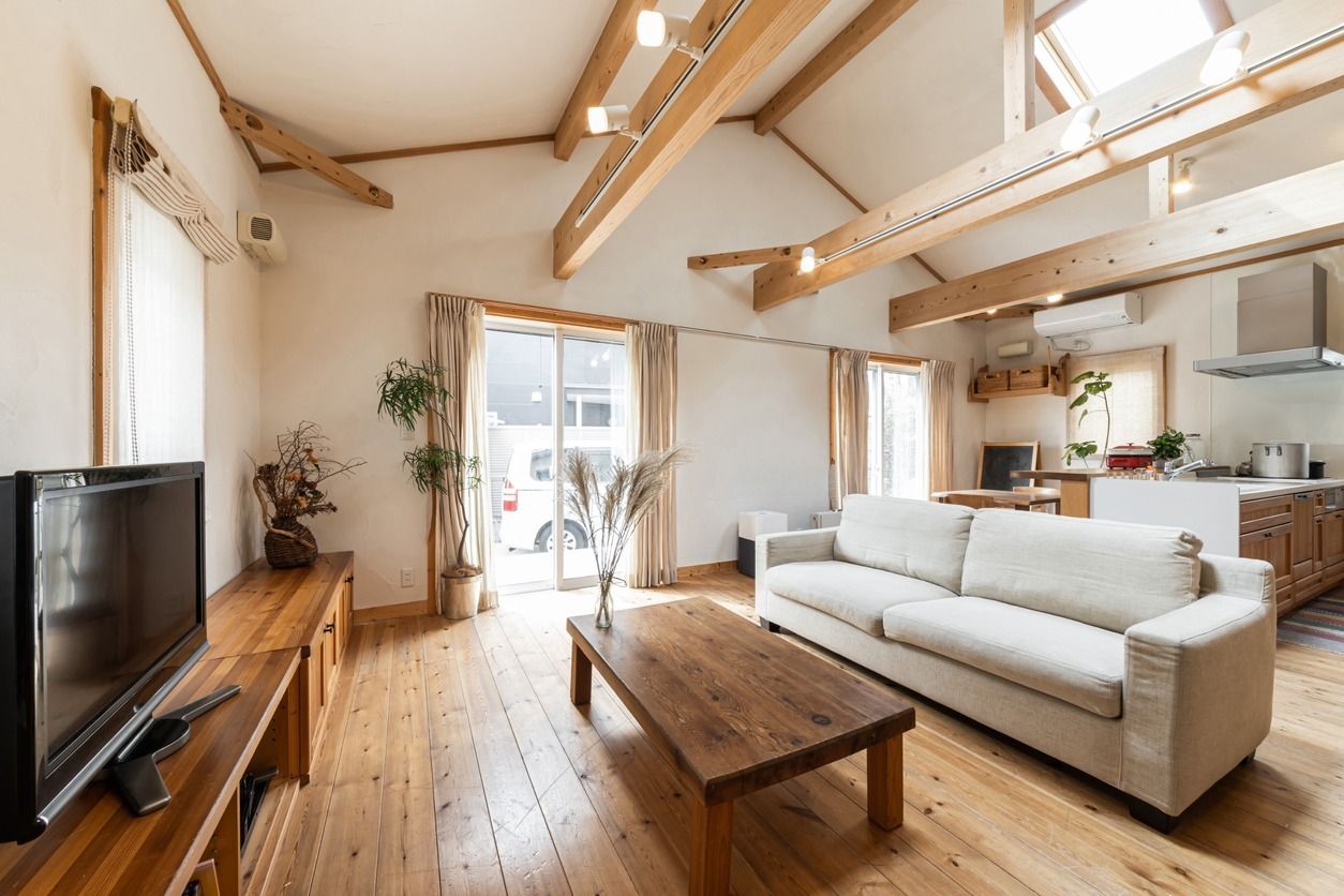 Sala de estar con suelo de madera, sofá blanco, mesa de centro de madera y vigas a la vista.