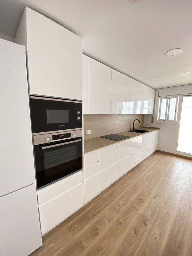 Una cocina con gabinetes blancos, electrodomésticos de acero inoxidable y pisos de madera.