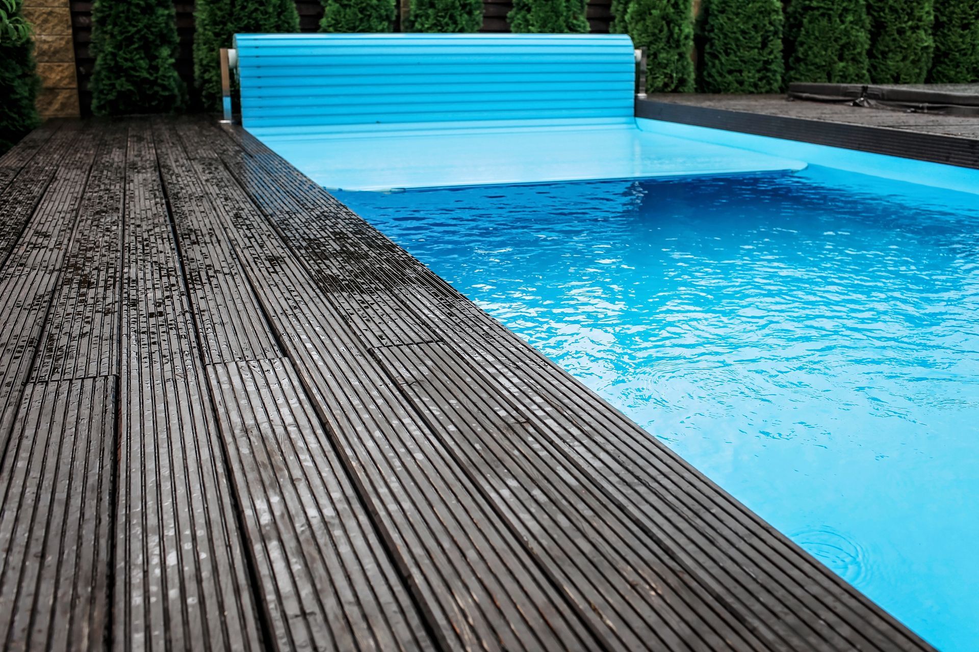 Terrasse en bois jouxtant une piscine rectangulaire à l'eau bleue et couverte.