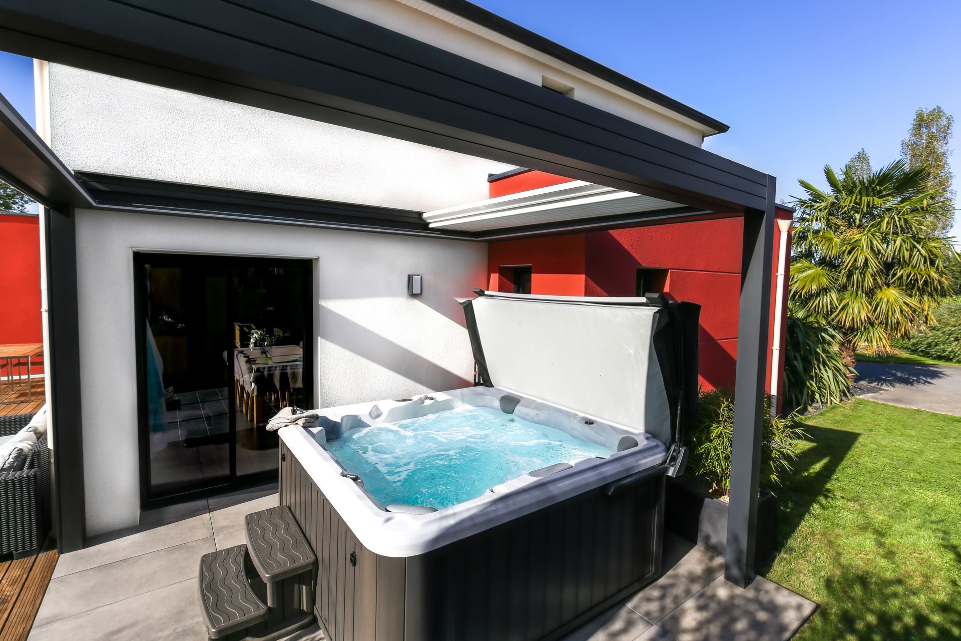 Une piscine rectangulaire entourée d'une couverture transparente, située dans un jardin avec une maison en pierre.