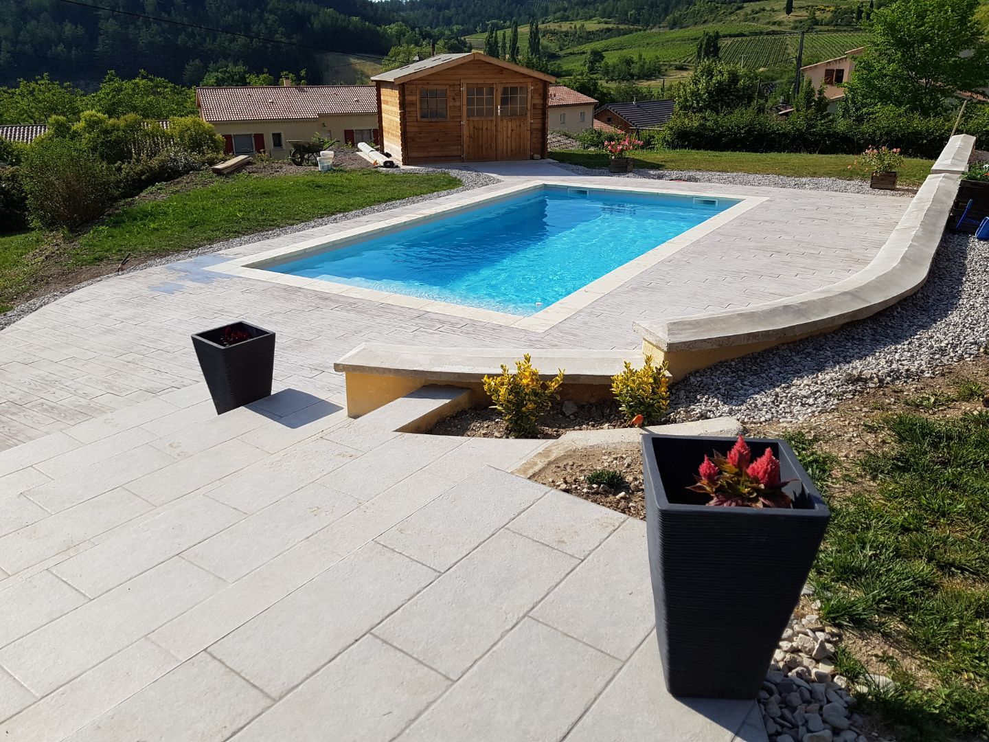 Piscine extérieure ensoleillée avec abri en bois et terrasse en pierre.