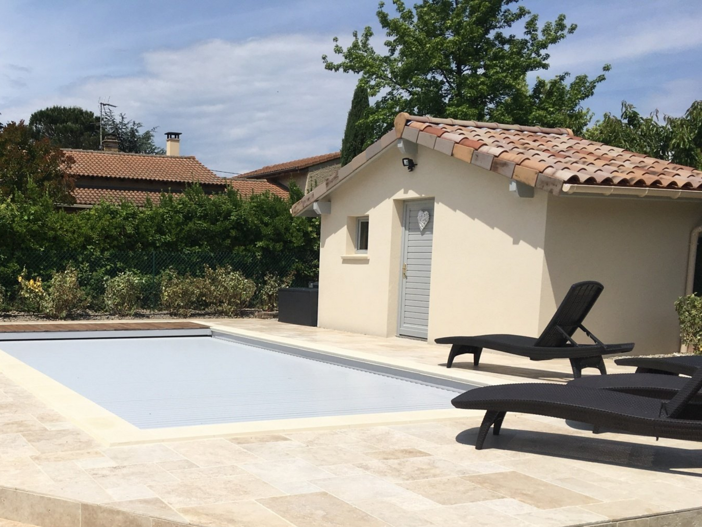 Piscine avec un petit bâtiment beige et deux chaises longues.